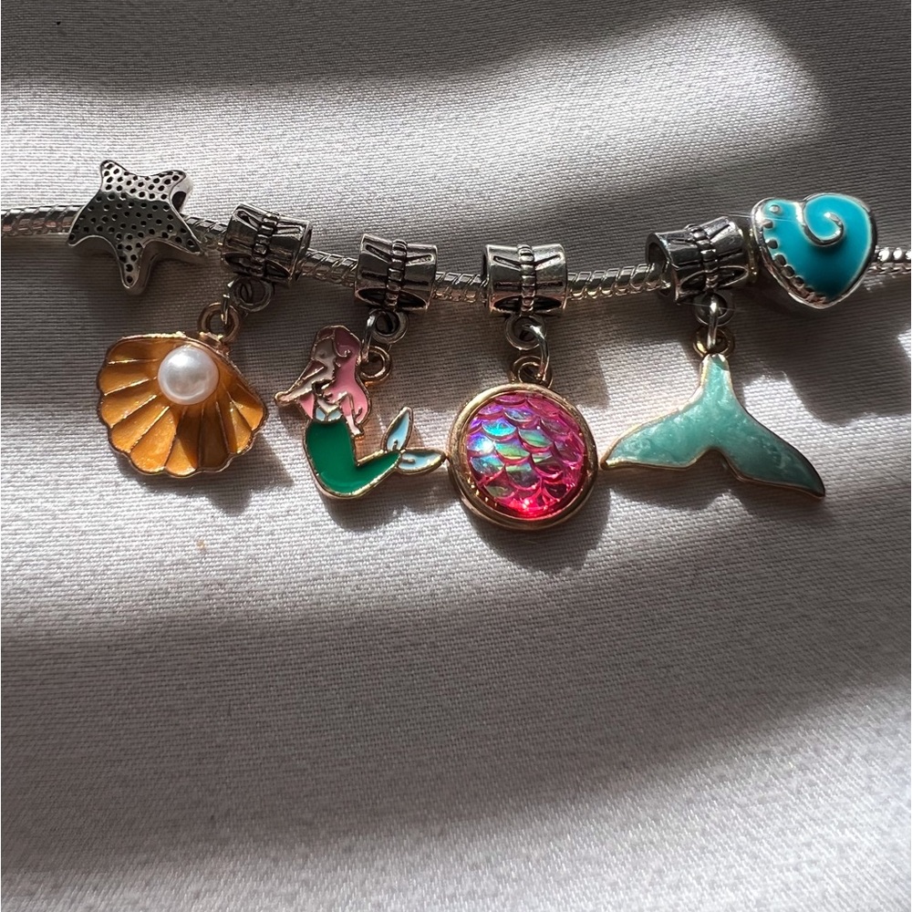 Silver charm bracelet with mermaid themed charms .
